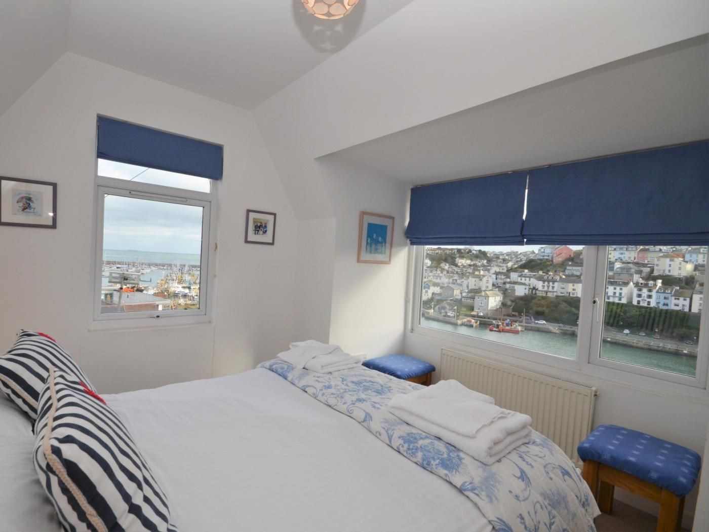 A bedroom with a large bed, two windows with views of a town, and a radiator.