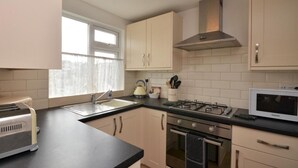 A modern kitchen with a gas stove, oven, microwave, and a window with curtains. - 3 Bed in Brixham (oc-bx018) (Brixham)