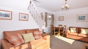 A living room with a sofa, a dining table with chairs, a chandelier, and a staircase. - 3 Bed in Brixham (oc-bx018) (Brixham)