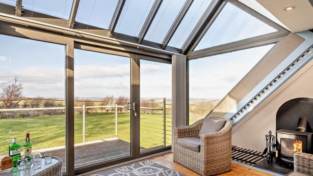 Ein modernes Interieur mit Glasdecke, Kamin, Korbmöbeln und Blick ins Grüne.