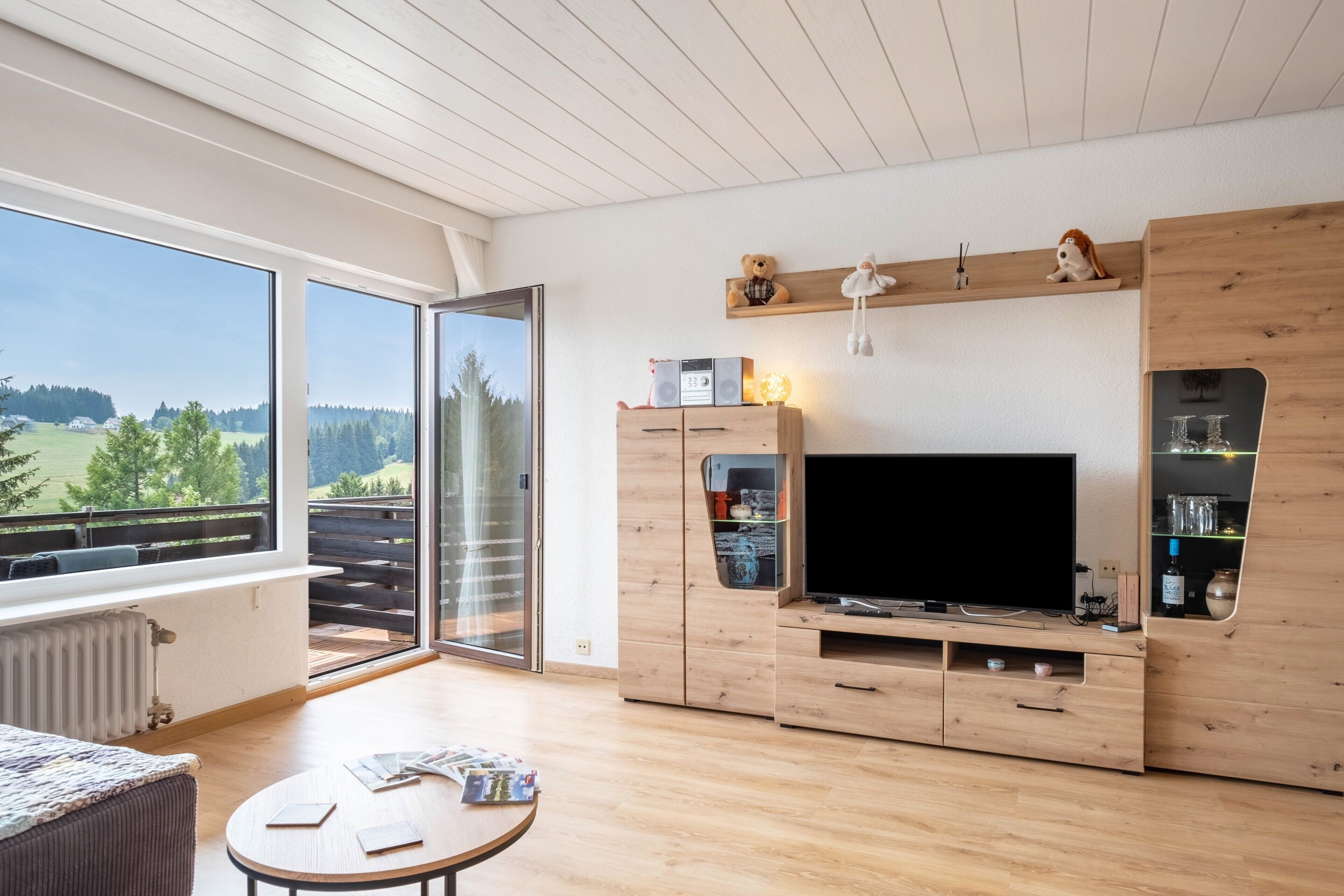 A modern living room with a large TV, wooden cabinets, and a sliding glass door leading to a balcony.