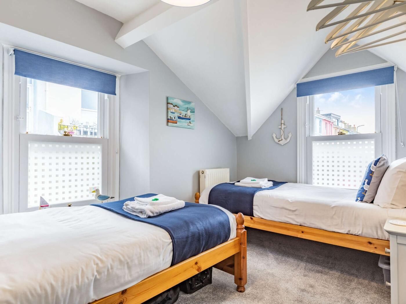 A bedroom with two beds, a window with a view, a painting on the wall, and a ceiling fan.