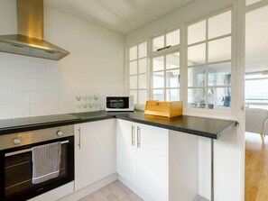 A kitchen with white cabinets, a microwave, a stove, and a window with a view. - 3 Bed in Brixham (oc-bx034) (Brixham)