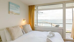 Ein Hotelzimmer mit einem Bett, einem Gemälde, einem Fenster mit Meerblick und einem Vorhang.