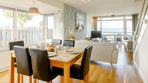 Ein modernes Wohnzimmer mit Essbereich, einer Wand aus Stein, einem Flachbildfernseher und Blick auf das Meer.