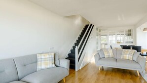 Ein großzügiger Wohnbereich mit grauem Sofa, einer Treppe und einem Essbereich im Hintergrund.