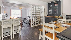 Een moderne keuken met witte kasten, een eettafel gedekt voor vier personen, en een ingebouwde boekenkast met een hartvormige decoratie.