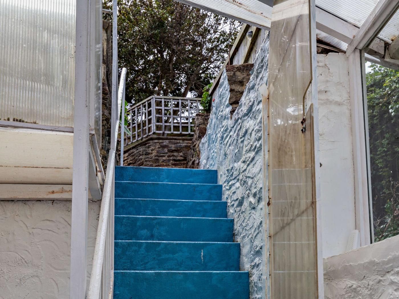 Una escalera con escalones azules que lleva a un muro de piedra con barandilla metálica.