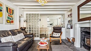 Een woonkamer met een leren bank, een houten salontafel met fruit, een open haard en een keuken op de achtergrond.