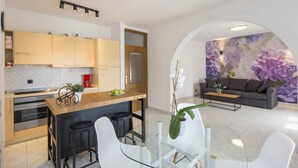 Eine moderne Küche mit einer Holztischinsel, schwarzen Barhocker und einem Essbereich mit Glastisch und weißen Stühlen.