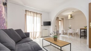 Ein modernes Wohnzimmer mit einer Couch, einem Couchtisch, einem Fernseher und einem Essbereich mit Stühlen und einem Tisch.