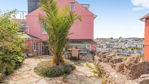 Un bâtiment rose avec un chemin de pierre, un palmier et une vue sur une ville côtière.