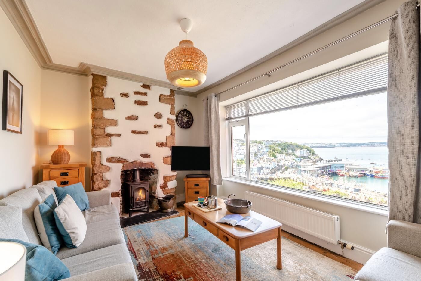 A living room with a stone wall, a fireplace, a sofa, a coffee table, and a view of the sea.