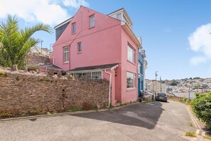 Una casa rosa amb mur de pedra, un cotxe estacionat al davant i vista d'una vila situada en un turó.