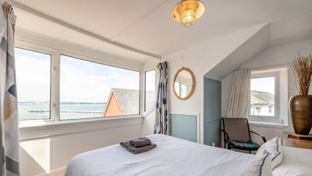 Une chambre à coucher avec un lit, une chaise, un miroir et une vue sur la mer.