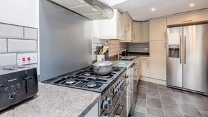 Une cuisine moderne équipée d’une cuisinière à gaz, d’un four, d’un réfrigérateur en acier inoxydable et d’une hotte intégrée.