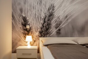 Une chambre à coucher avec un lit, des oreillers, une table de chevet, une lampe et un mur orné d’un motif représentant des tiges de blé.