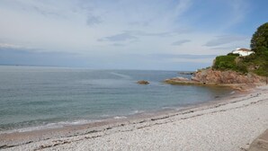 Ein Küstenstrand mit felsigem Ufer, ein weißes Gebäude auf einer Klippe und ruhiges Meer.
