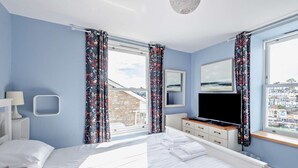 Ein Schlafzimmer mit einem Bett, einem Fernseher, einem Schminktisch und einem Fenster mit Vorhängen.