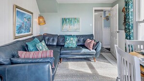 Ein Wohnzimmer mit einem Ecksofa, einem gemusterten Teppich und Kunstwerken an den Wänden.