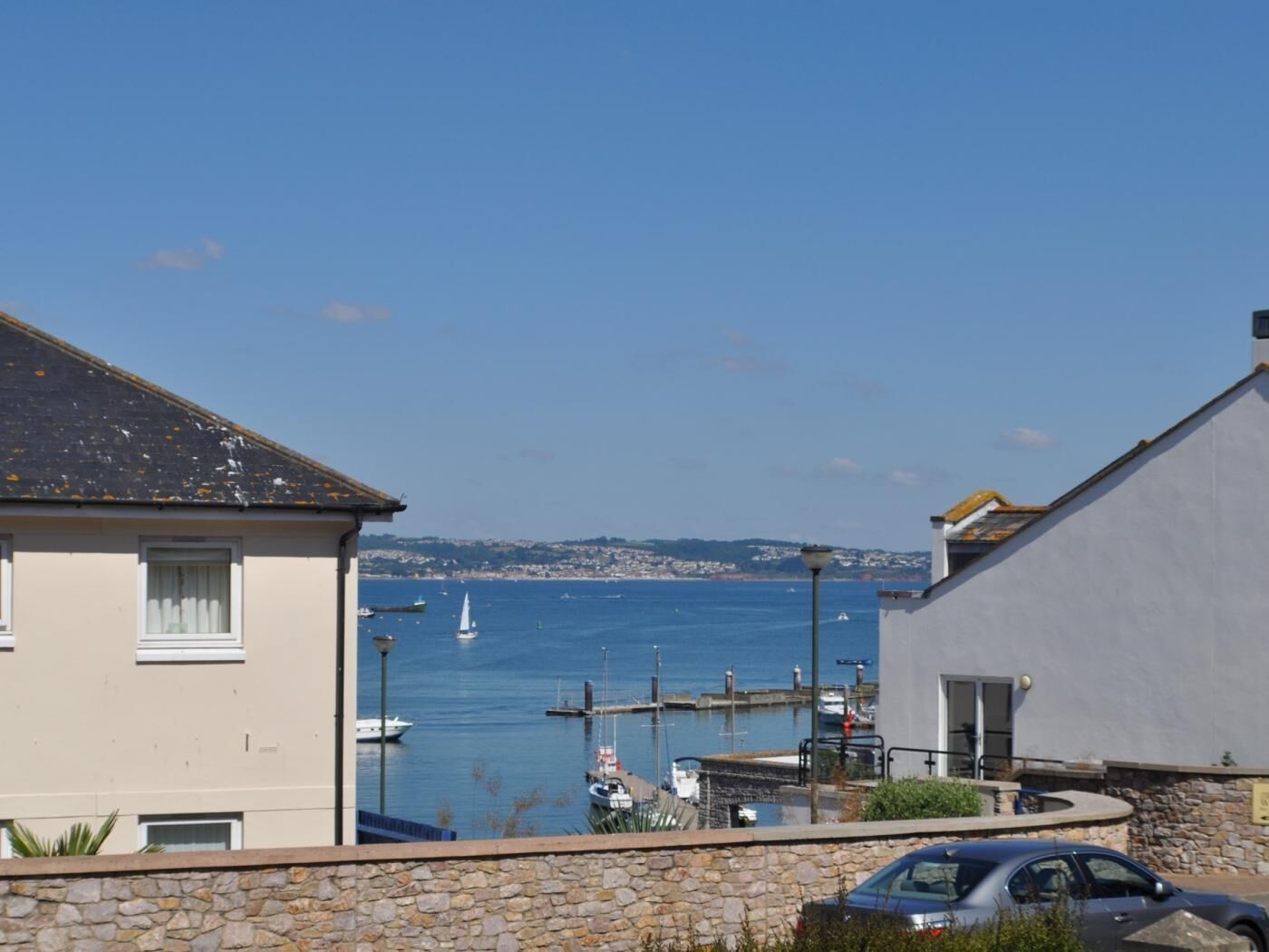 A coastal view with a marina, stone wall, and a building with a flat roof.