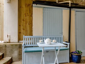 Un banco de madera blanca con una mesa, una tetera blanca y una taza.