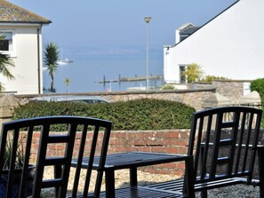 Un patio frente al mar con dos sillas de metal negro, un edificio blanco y vistas al océano.
