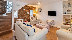 Una sala de estar con pared de piedra, una escalera, un televisor y una estantería.