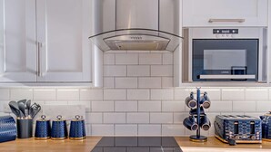 Eine moderne Küche mit weißen Schränken, einem eingebauten Backofen, einer Dunstabzugshaube aus Glas und einer Arbeitsplatte mit einem schwarzen Induktionskochfeld.