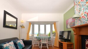 Uma sala de estar com sofá, uma mesa de jantar com cadeiras, televisão e lareira.