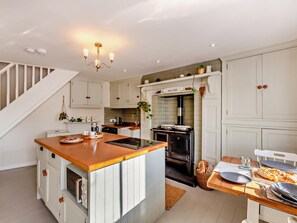 A kitchen with a central island, a stove, and a dining area with a table set for two. - 1 Bed in Brixham (oc-bx036) (Brixham)