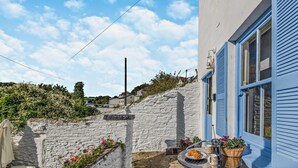 Un'area esterna con tavolino e sedie, un muro di pietra bianca e un edificio azzurro con persiane.