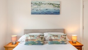 Ein Schlafzimmer mit einem Bett, zwei Nachttischlampen und einem Bild einer Küstenlandschaft über dem Bett.