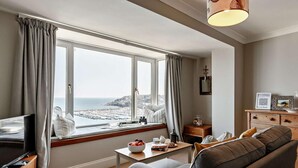 Ett rum med ett stort fönster, en soffa, ett soffbord, en tv och ett träskåp.