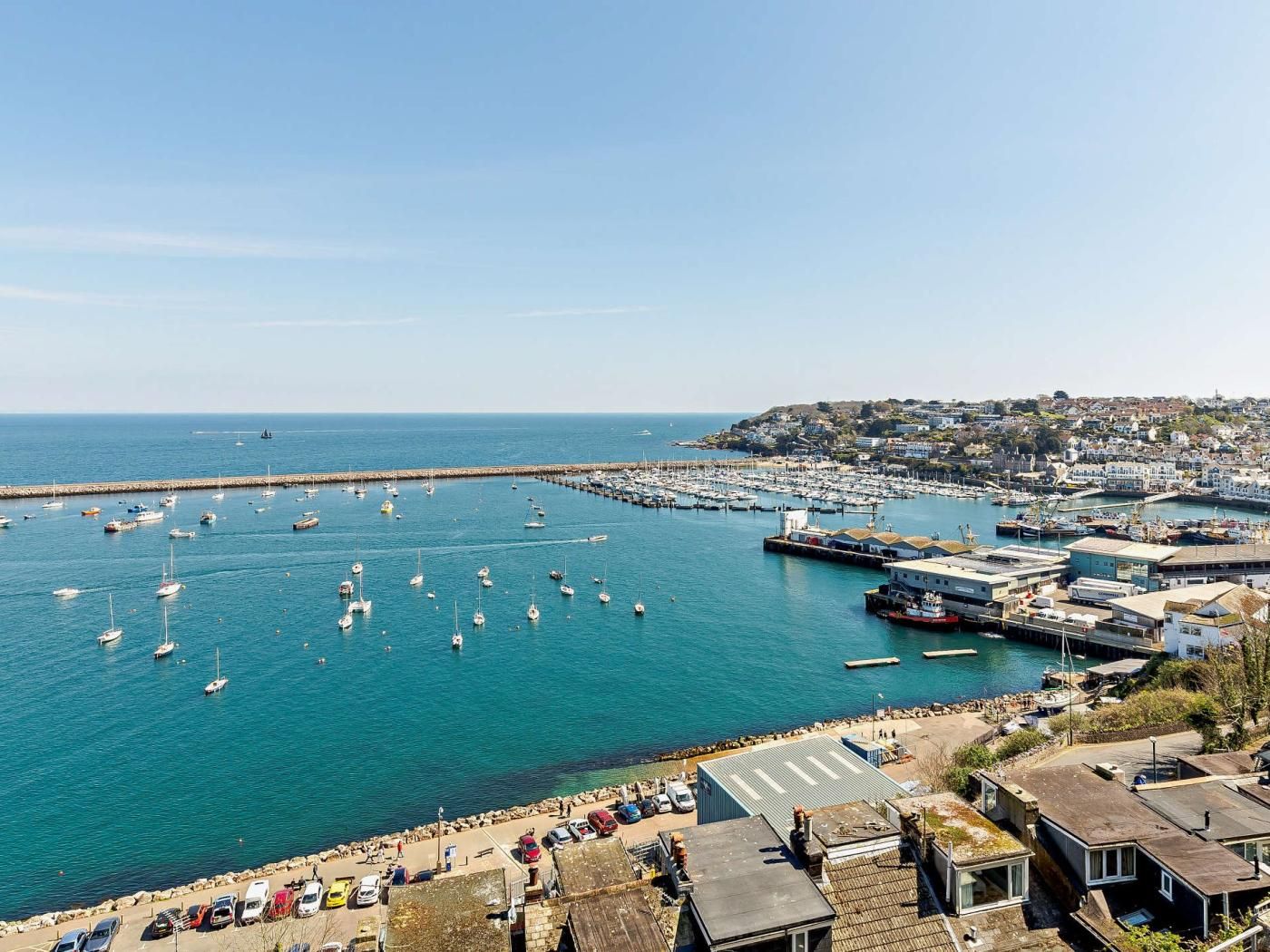 A coastal town with a marina filled with boats, a pier, and residential buildings.