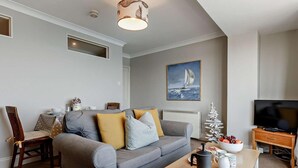 Ett vardagsrum med en grå soffa, ett soffbord i trä, en tv och en målning av en segelbåt på väggen.