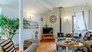A living room with a TV, a fireplace, a sofa, and a dining table with food. - 2 Bed in Brixham (oc-bx083) (Brixham)