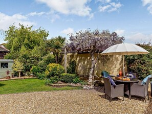 Un jardín con una mesa y sillas, una pérgola y un muro de piedra.