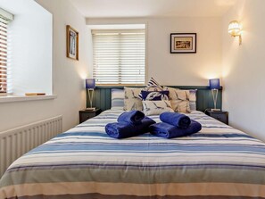 Una cama bien hecha con ropa de cama a rayas, dos lámparas de noche y un cuadro en la pared.