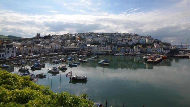 A coastal town with a harbor filled with boats, a prominent church on a hill, and a mix of residential buildings. - 2 Bed in Brixham (oc-bx083) (Brixham)