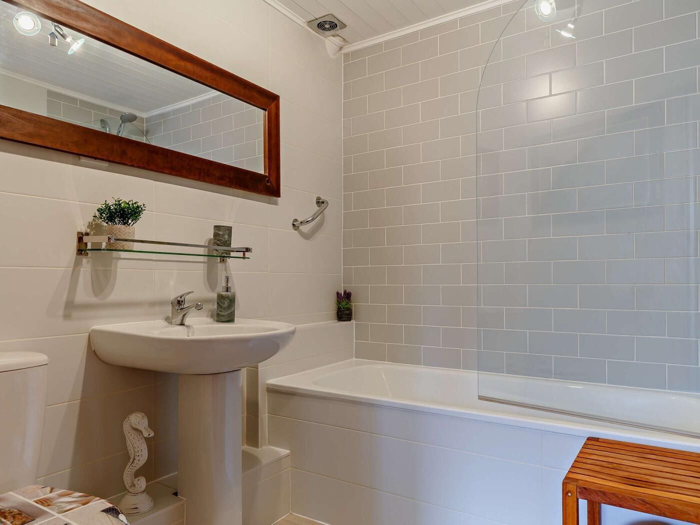 A bathroom with a white sink, a mirror, a bathtub, and a wooden stool.
