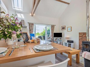 Comedor con mesa de madera preparada para dos personas, un jarrón de flores y vista al exterior.