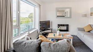 Ein Wohnzimmer mit Sofa, Fernseher, Couchtisch und Blick auf Grünflächen.