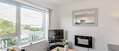 Una sala de estar moderna con televisor, chimenea y ventanas amplias con vistas a un paisaje verde.