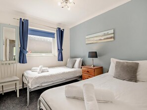 Ein Hotelzimmer mit zwei Betten, einem Nachttisch, einer Lampe, einem Fenster mit Vorhängen, einem Heizkörper und einem Bild an der Wand.