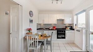 Eine kleine Küche mit weißen Schränken, einer gefliesten Spritzschutzwand und einem Essbereich mit Holztisch und -stühlen.
