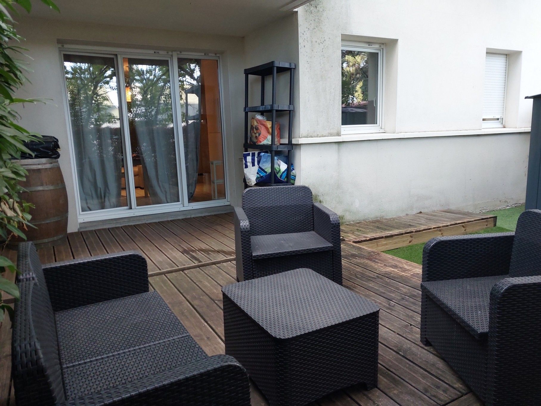 Un espace extérieur aménagé en terrasse, avec des meubles en osier, une porte-fenêtre coulissante et une petite bibliothèque.
