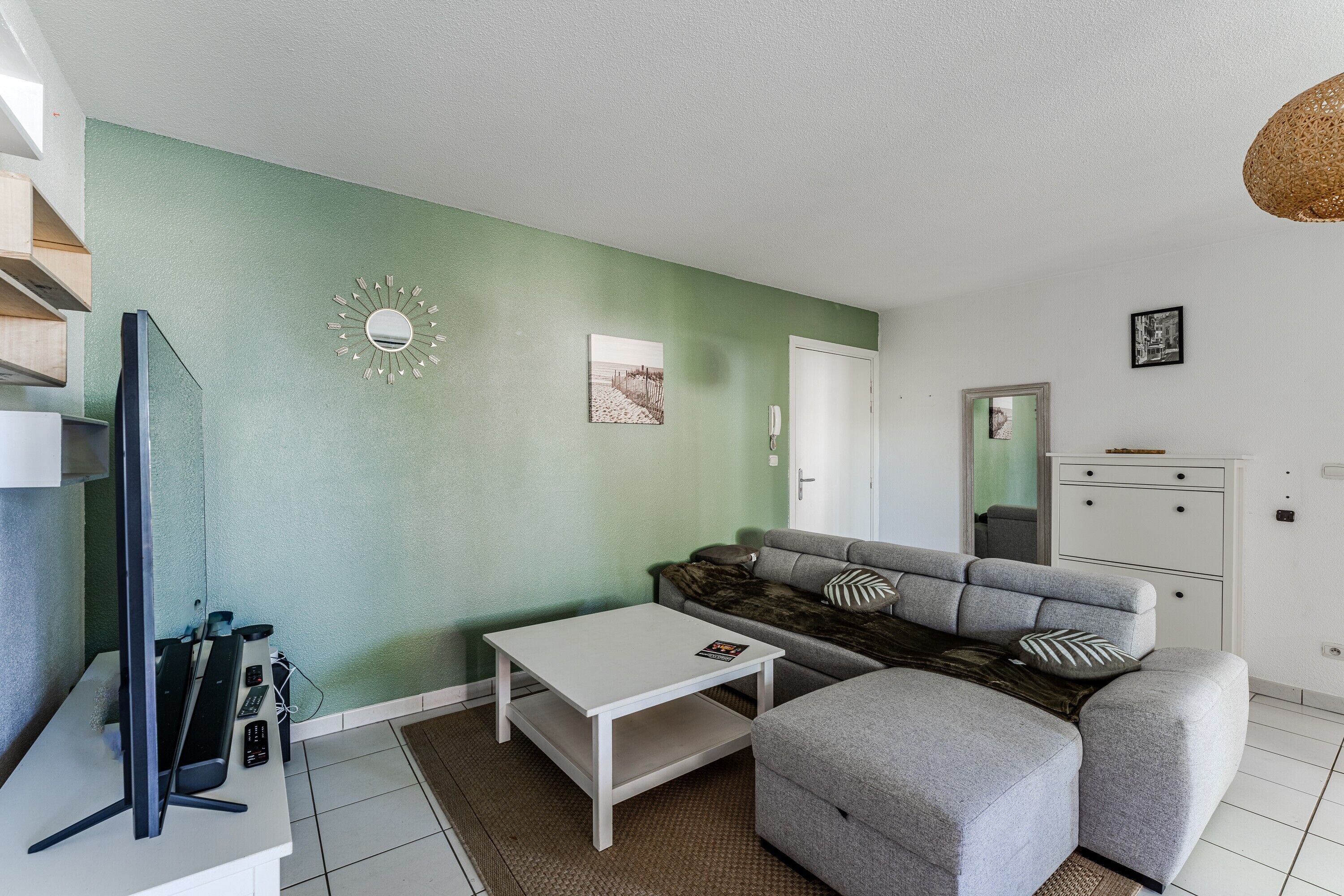 Een moderne woonkamer met een groene accentmuur, een grijze bank, een witte salontafel en een flatscreen-televisie.