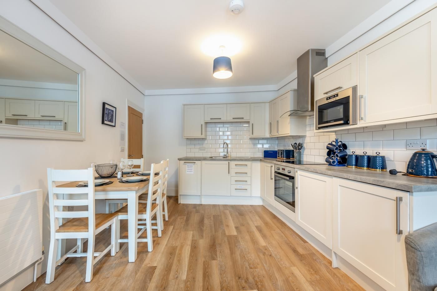 A compact kitchen with white cabinetry, a dining table with chairs, a microwave, an oven, and a kettle.