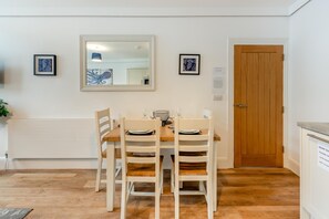 A dining area with a wooden table and chairs, a mirror on the wall, and a wooden door. - 2 Bed in Brixham (oc-54679) (Brixham)